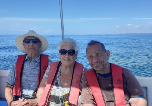 Two men and one women, on a boat trip. They are wearing lifejackets and the blue sea is behind them filling the background.