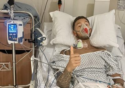Young man laying in a hospital bed give a thumbs up.