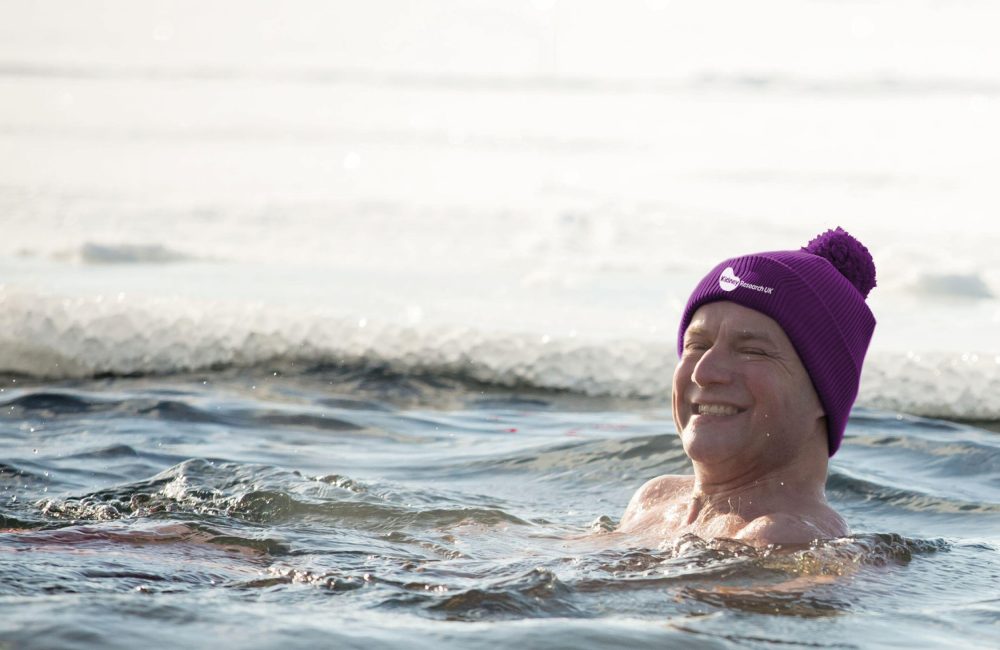 Male swimming on his back in the sea, he is wearing a purple bobble hat