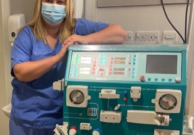 Female wearing blue scrubs and a face mask next to a some hospital equipment