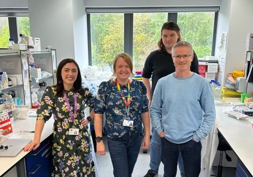 The research team, two females and two males, standing together in their research lab.