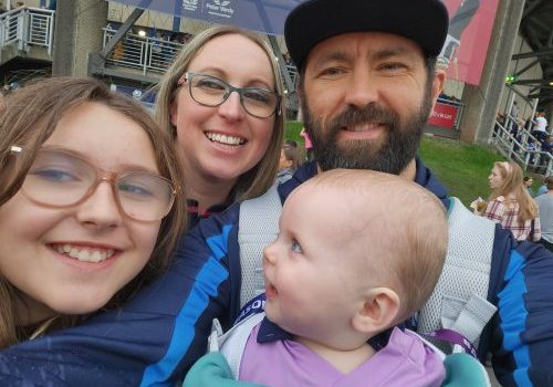 Grant wearing a cap with a beard, standing with wife and daughter and baby