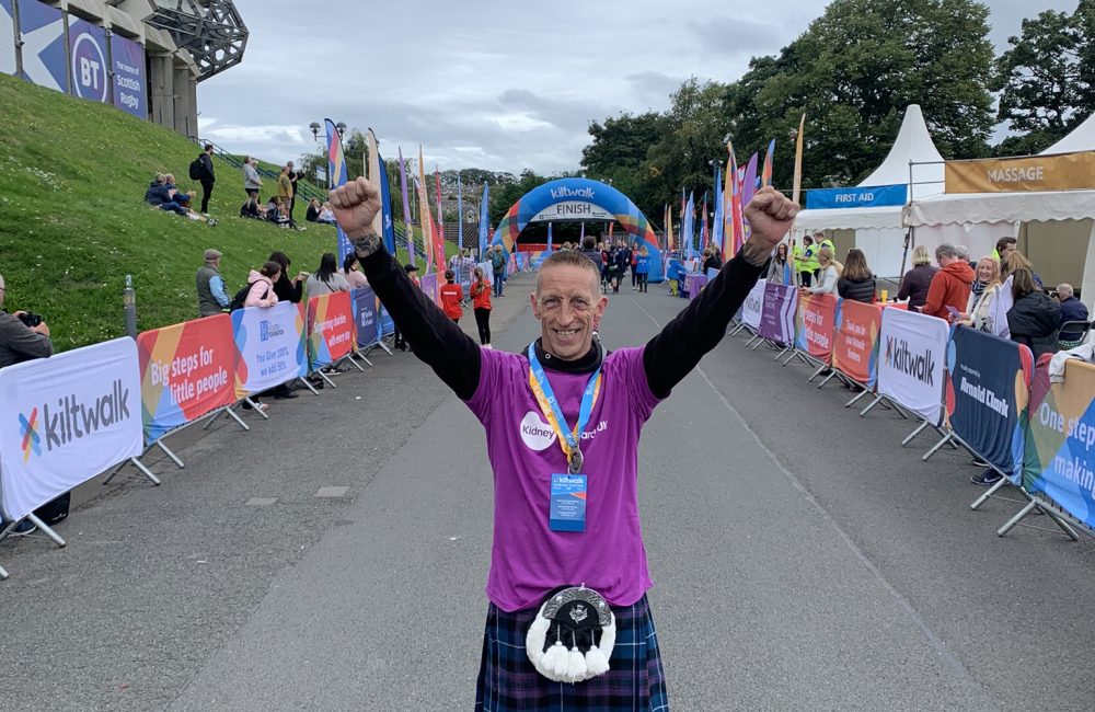 Man wearing a kilt and Kidney Research UK tshirt with arms in the air