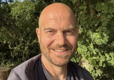 Tim, in the garden, taking a selfie smiling for the camera.