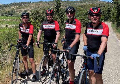 Tim Blackburn four men wearing the same red and black cycling kit, standing next to their bikes, with blue skies behind them.
