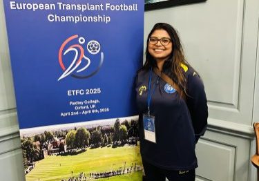 Jelina wearing her team tracksuit standing next to European Transplant Football pull up banner
