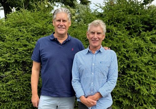 Brothers standing side by side in front of some fir trees.
