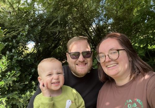 Keven Rudd, Alanah and Flynn Family selfie of dad, mum and small boym with hedge and trees in the background.
