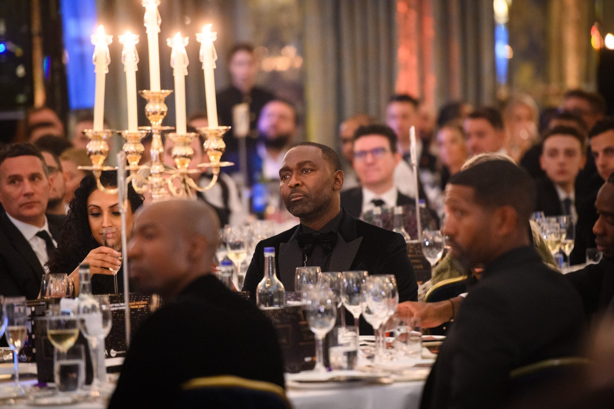 Group of men sat at a table at the gala event with wine glasses and candelabra in front of them