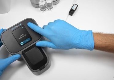 Hands wearing blue latex gloves holding a Quick Check device