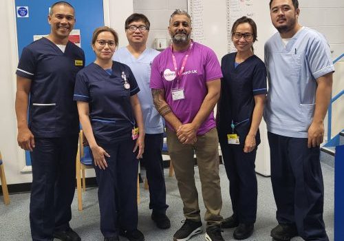 Paul, wearing his Kidney Research UK branded t-shirt. standing with five renal unit staff who are all wearing their blue hospital uniforms.