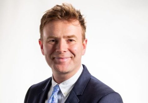 Rhys Evans Head and shoulders picture of a man wearing a suit, white shirt and blue tie, smiling for the camera.