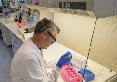 scientific photo Male researcher working at a bench, wearing blue gloves and white coat, holding a pipette