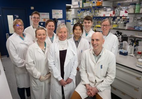 staff and students in a group shot in the lab, all are wearing white lab coats.