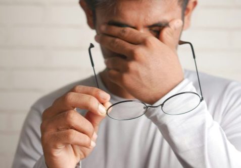 Man rubbing eyes and holding his glasses