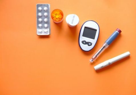 insulin pen, diabetic measurement tools and pills on orange background