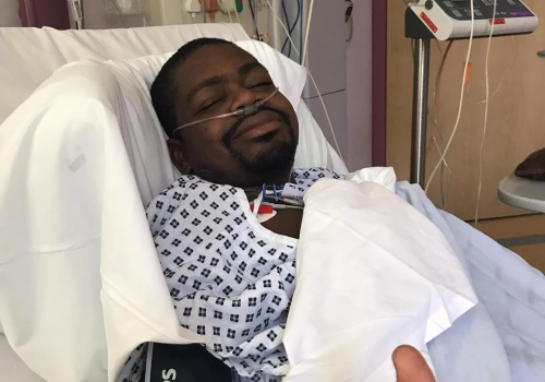 Man in hospital bed, giving a thumbs up.