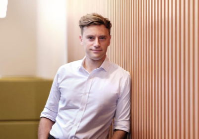 A male, wearing a white shirt, leaning up against a wall