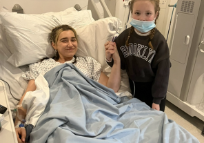 Female in hospital bed with young girl standing next to the bed holding her hand.