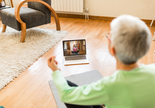 Person sitting on floor crossed legged, with back to the camera. Laptop in front on the floor showing exercises.