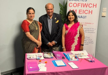 Two south Asian women with a male standing behind a presentation table