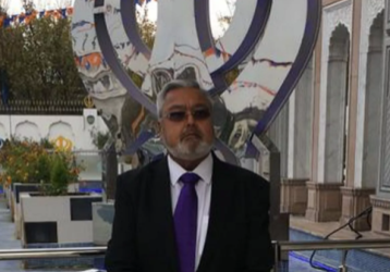 Sam, wearing a suit and glasses, with the Gurdwara behind him