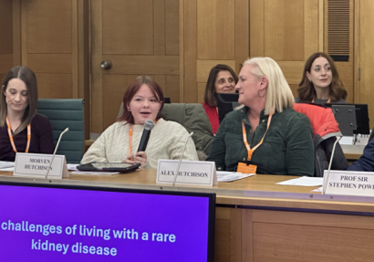 Young adult sitting on panel alongside two women and one man. The young adult is speaking into a microphone.
