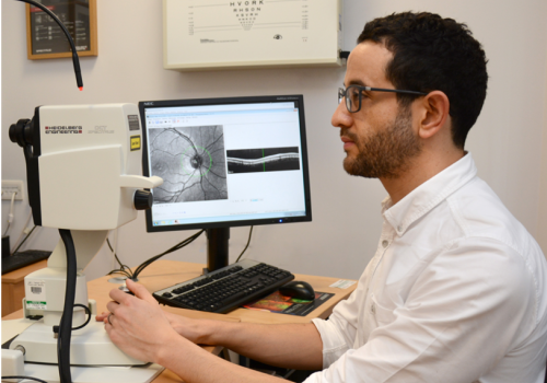 Man sat at a desk, with a computer monitor showing which a scan of an eye image.